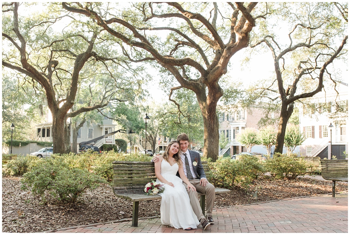 bride and groom sitting on bench with oak trees