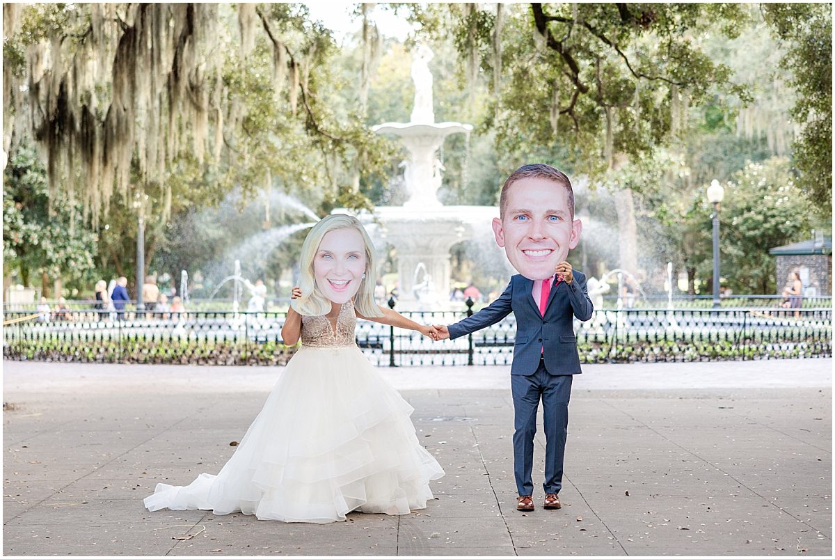 bride and groom in front of forsyth park fountain holding big heads up to cover their faces by savannah wedding photographer amber elizabeth weddings